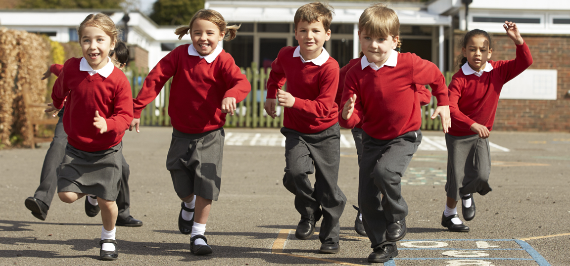 Five primary school aged children in red jumpers and grey trousers or skirts, running on a school playground. Please note this is a generic stock image.