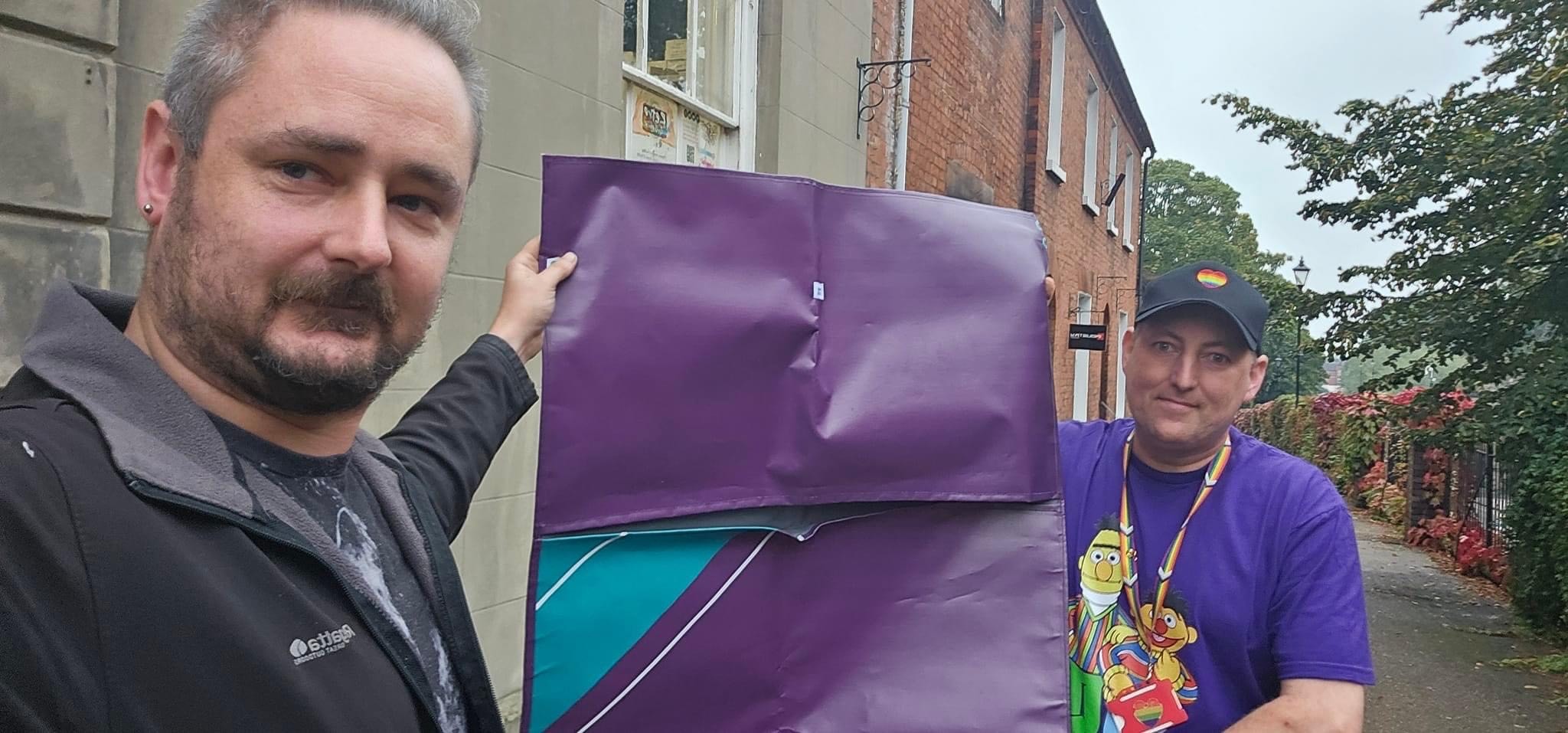 Two people holding up a purple sleeping bag shell