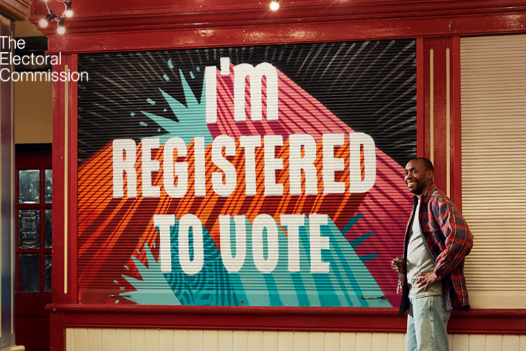 A wall with the text 'I'm registered to vote' and a person stood next to it smiling