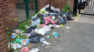 A lot of fly-tipped waste on the ground outside buildings