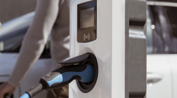 image of a EV charging point with a person standing next to it by a white car