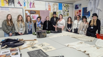 photo of a group of students in a classroom standing by a textiles table 