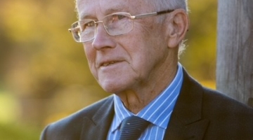 photo of a man with grey hair, glasses and wearing a blue shirt, tie and dark jacket
